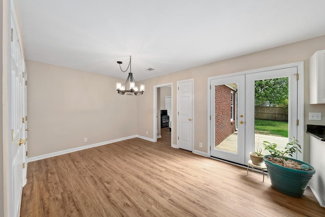 unfurnished dining area featuring visible vents, baseboards, light wood-type flooring, a chandelier, and french doors