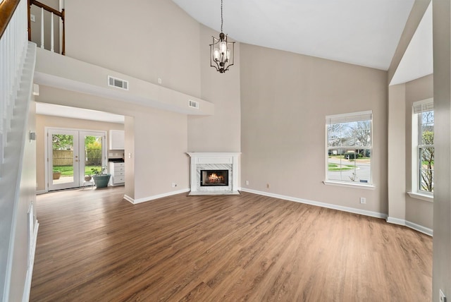 unfurnished living room with visible vents, plenty of natural light, a high end fireplace, wood finished floors, and high vaulted ceiling