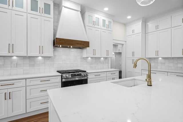 kitchen featuring white cabinets, gas range, a sink, premium range hood, and decorative backsplash