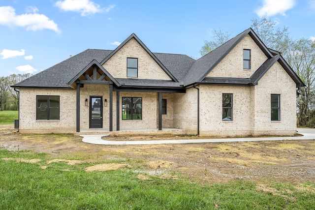 view of front facade featuring roof with shingles, a front yard, and brick siding