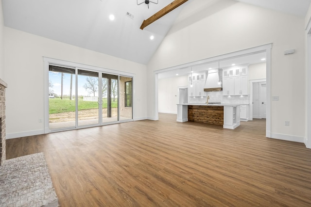 unfurnished living room with a fireplace, visible vents, high vaulted ceiling, a sink, and wood finished floors