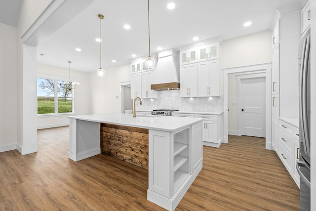 kitchen featuring custom exhaust hood, white cabinetry, a center island with sink, decorative backsplash, and a sink