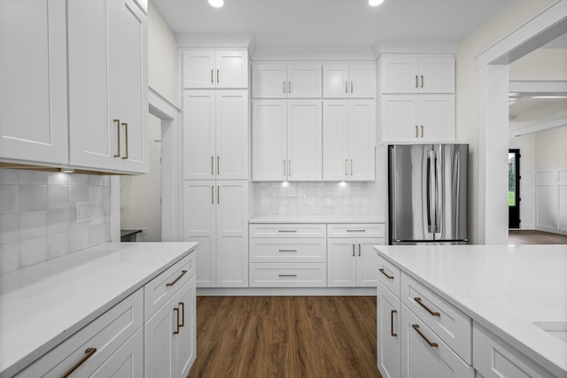 kitchen with freestanding refrigerator, light stone countertops, dark wood-type flooring, white cabinetry, and backsplash