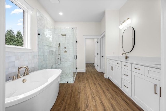full bath featuring tile walls, a soaking tub, a shower stall, vanity, and wood finished floors