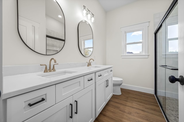 full bathroom with toilet, wood finished floors, a sink, double vanity, and baseboards