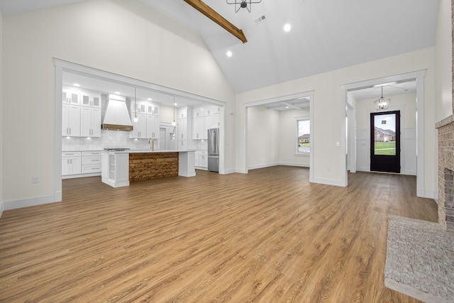 unfurnished living room with light wood-type flooring, baseboards, visible vents, beam ceiling, and high vaulted ceiling