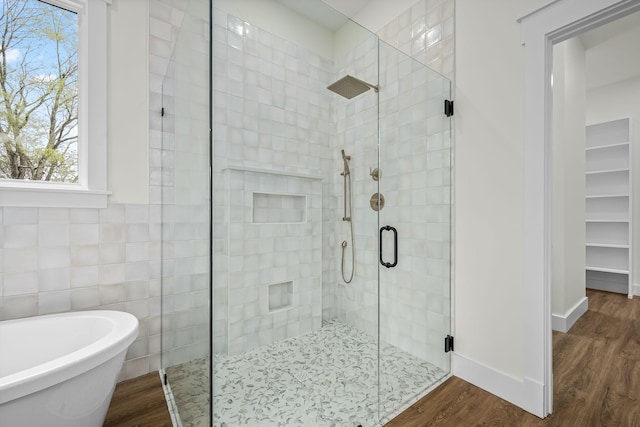 full bathroom with a shower stall, a freestanding bath, tile walls, and wood finished floors