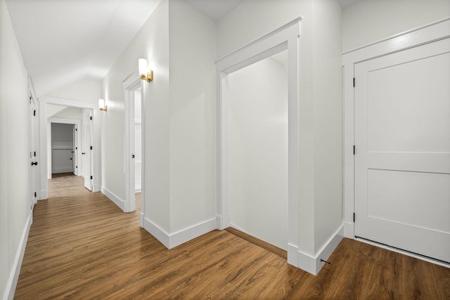 hallway featuring wood finished floors, baseboards, and lofted ceiling
