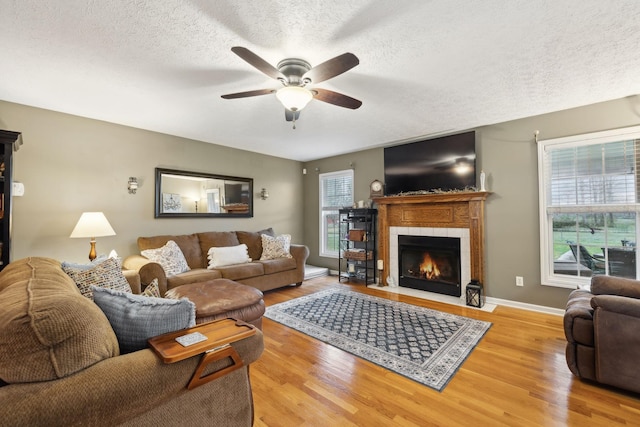 living area featuring a tiled fireplace, ceiling fan, a textured ceiling, and wood finished floors