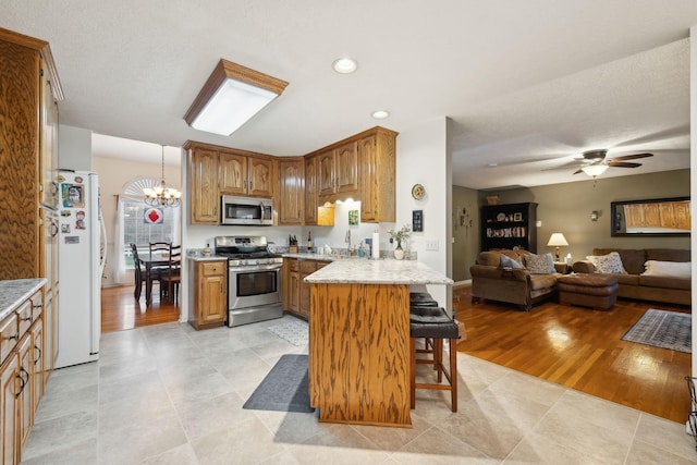 kitchen featuring a kitchen breakfast bar, a peninsula, open floor plan, stainless steel appliances, and ceiling fan with notable chandelier