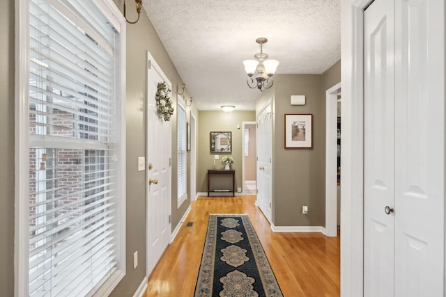 corridor with a textured ceiling, visible vents, a chandelier, light wood finished floors, and baseboards