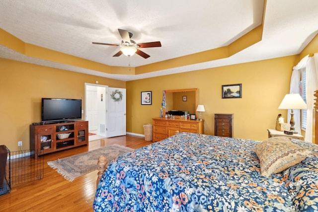 bedroom with baseboards, a ceiling fan, a textured ceiling, a tray ceiling, and wood finished floors