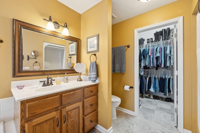 full bathroom with toilet, vanity, baseboards, and a walk in closet