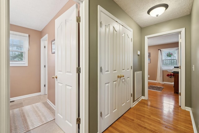 hall with visible vents, baseboards, light wood-type flooring, and a textured ceiling