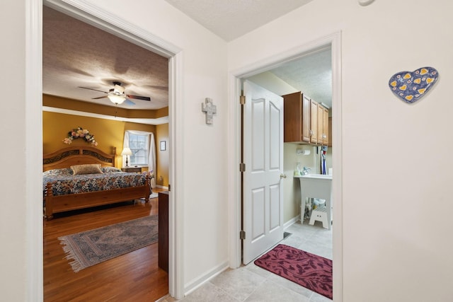 bedroom featuring baseboards, a ceiling fan, light tile patterned flooring, and a textured ceiling