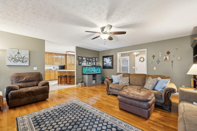living room with a textured ceiling, light wood finished floors, and ceiling fan with notable chandelier