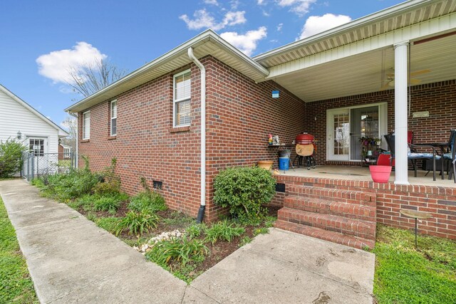view of exterior entry with a porch, brick siding, and crawl space