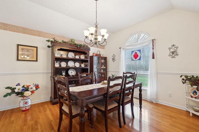 dining space with a notable chandelier, light wood-type flooring, baseboards, and lofted ceiling
