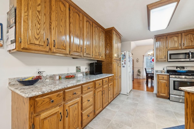 kitchen featuring brown cabinets, light stone countertops, and stainless steel appliances