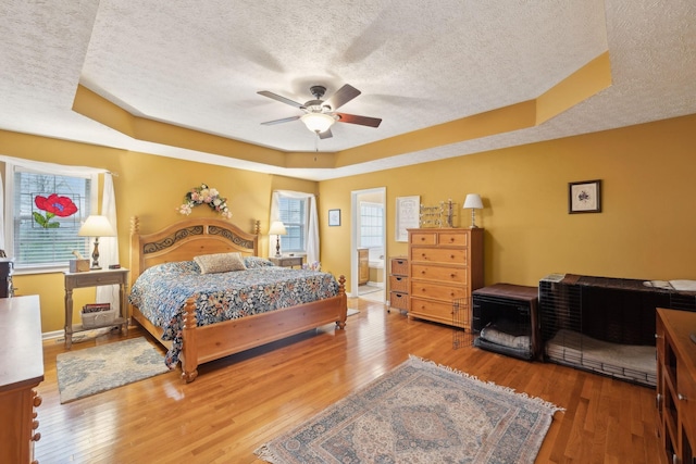 bedroom with a tray ceiling, a textured ceiling, wood-type flooring, and baseboards