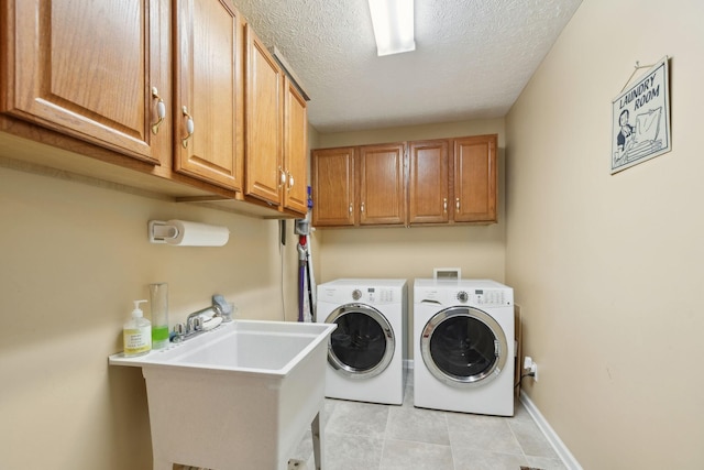 washroom featuring a textured ceiling, washing machine and clothes dryer, a sink, baseboards, and cabinet space