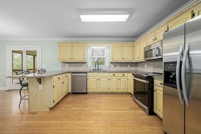 kitchen featuring ornamental molding, a peninsula, a kitchen bar, appliances with stainless steel finishes, and a sink