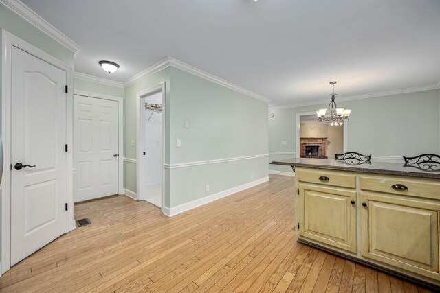 kitchen with ornamental molding, light wood-type flooring, dark countertops, and an inviting chandelier