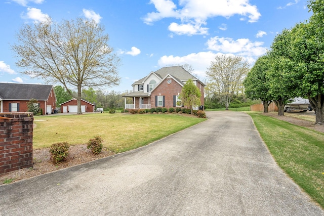 view of front facade featuring aphalt driveway, a detached garage, an outdoor structure, a front lawn, and brick siding