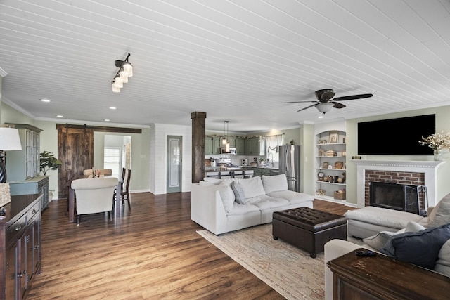 living room with a barn door, a ceiling fan, wood finished floors, a fireplace, and ornamental molding