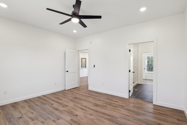 unfurnished bedroom with recessed lighting, baseboards, wood finished floors, and ensuite bathroom