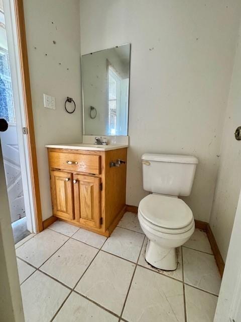 half bathroom with toilet, vanity, baseboards, and tile patterned flooring