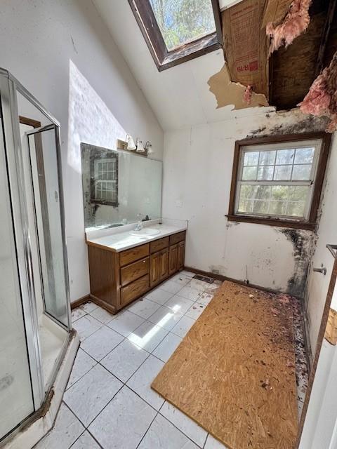 bathroom featuring vaulted ceiling with skylight, baseboards, a shower stall, vanity, and tile patterned flooring