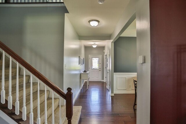entrance foyer with a decorative wall, a wainscoted wall, stairs, and dark wood finished floors