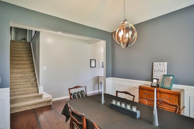 dining space featuring dark wood-type flooring, a notable chandelier, wainscoting, and stairs