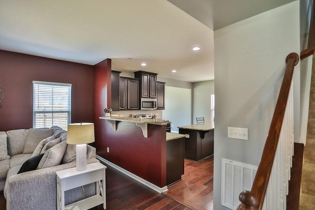 kitchen featuring visible vents, a breakfast bar, stainless steel microwave, light stone countertops, and dark wood-type flooring