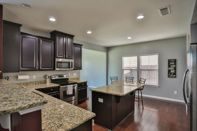 kitchen with visible vents, dark wood-style flooring, a kitchen breakfast bar, light stone countertops, and stainless steel appliances