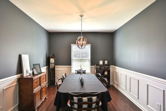 dining space featuring a chandelier, a decorative wall, dark wood finished floors, and a wainscoted wall