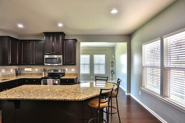 kitchen featuring appliances with stainless steel finishes, plenty of natural light, a kitchen bar, and light stone countertops