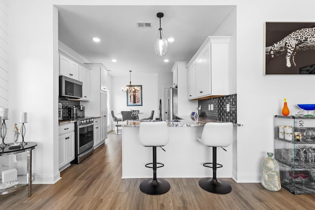 kitchen featuring a peninsula, appliances with stainless steel finishes, wood finished floors, and visible vents