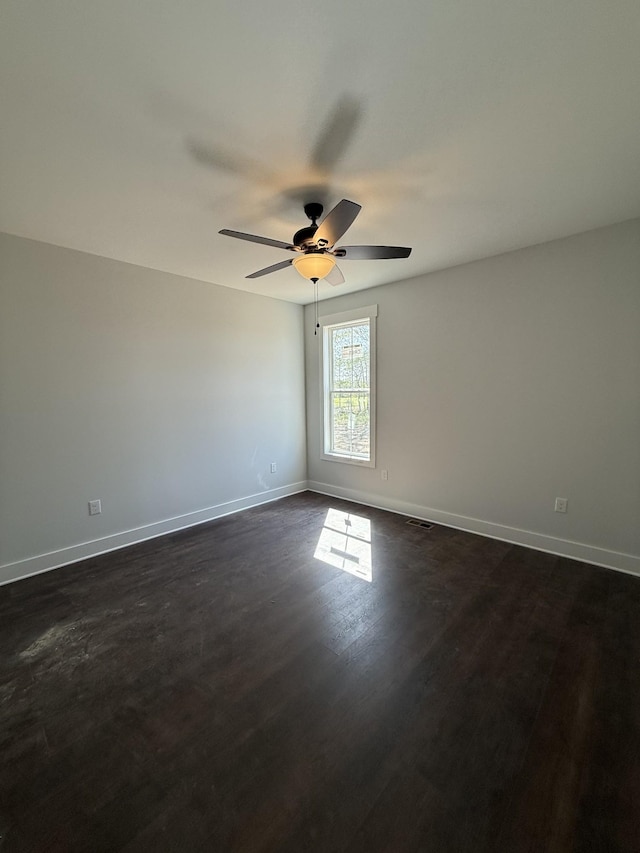 empty room featuring dark wood-type flooring, baseboards, a ceiling fan, and visible vents
