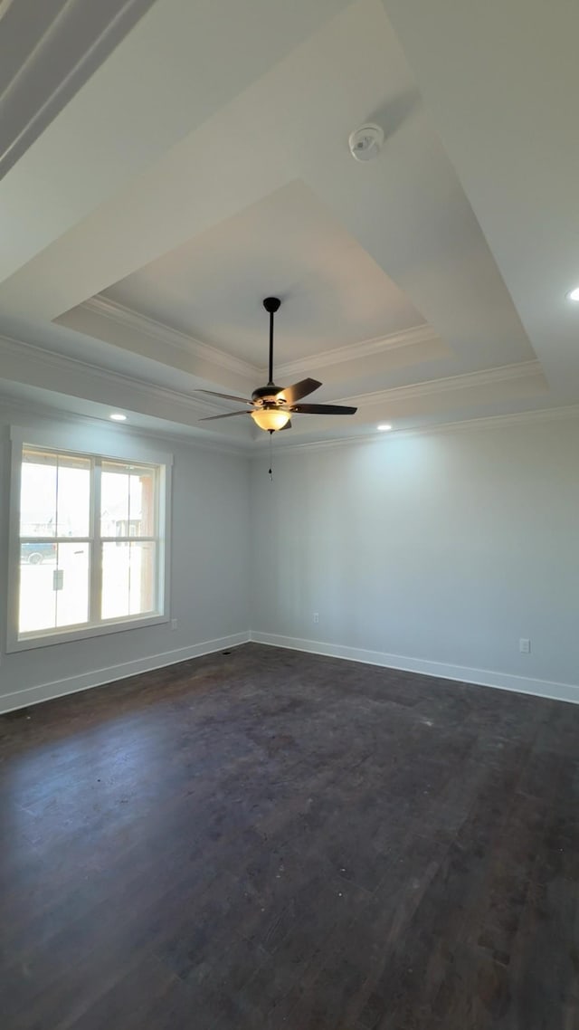 unfurnished room featuring a raised ceiling, crown molding, dark wood-style flooring, and baseboards