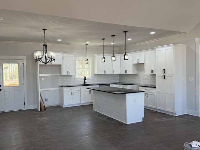 kitchen with a center island, a sink, ornamental molding, and dark countertops