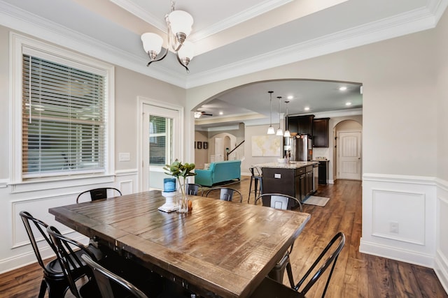 dining area with a tray ceiling, arched walkways, and an inviting chandelier