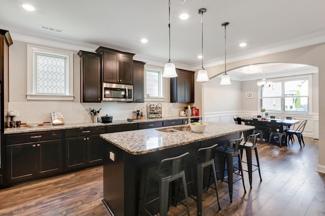 kitchen featuring stainless steel microwave, a breakfast bar, an inviting chandelier, crown molding, and a kitchen island with sink