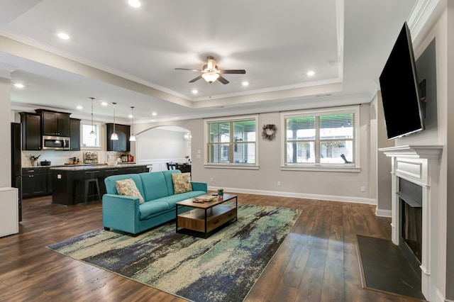living area featuring a healthy amount of sunlight, arched walkways, a fireplace, and ceiling fan