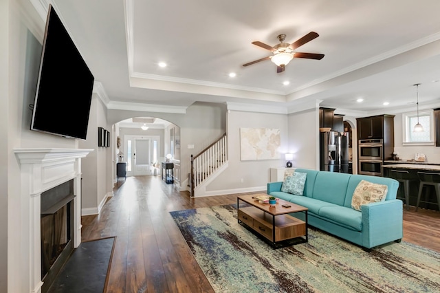 living room featuring baseboards, stairway, a ceiling fan, dark wood-type flooring, and arched walkways
