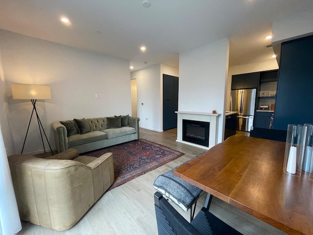 living area with recessed lighting, light wood finished floors, and a glass covered fireplace