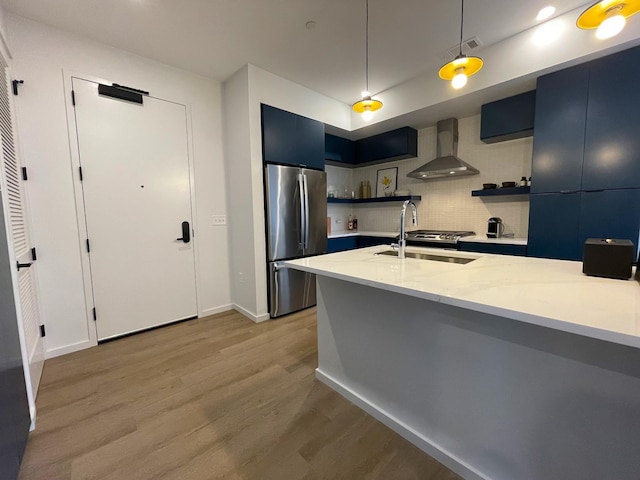 kitchen featuring wall chimney range hood, light wood-style flooring, freestanding refrigerator, open shelves, and a sink