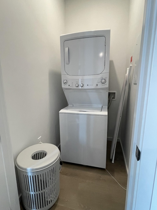 laundry room with baseboards, laundry area, wood finished floors, and stacked washer and clothes dryer