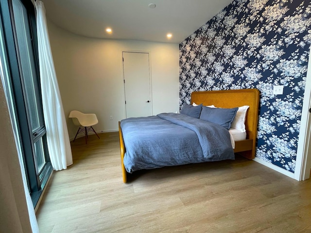 bedroom with an accent wall, recessed lighting, wallpapered walls, light wood finished floors, and baseboards